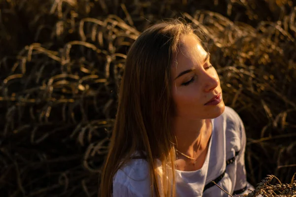 Genç bayan akşam güneşinin altında tarlada oturuyor.