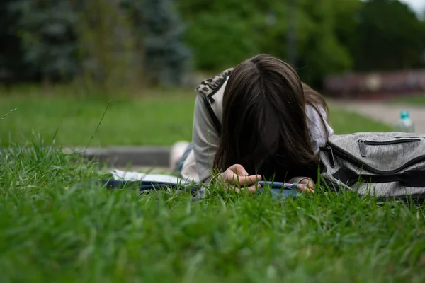 Koyu saçlı, cep telefonu yeşil çimlerde uzanan bir kız.