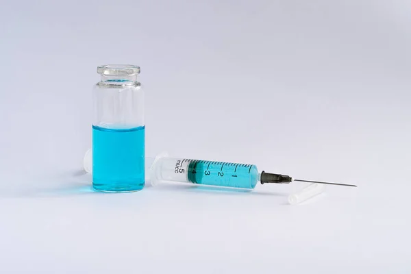 Medical bottle open in blue contents. A syringe with a needle is lying next to it.
