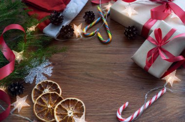 Üzerinde ladin dalı, hediyeler, tatlılar, portakallar ve bir çelenk olan koyu ahşap bir arka planda Noel kompozisyonu. Yukarıdan manzara. - Mutlu yıllar. Kırmızı kurdele. Metin için boşluk var.