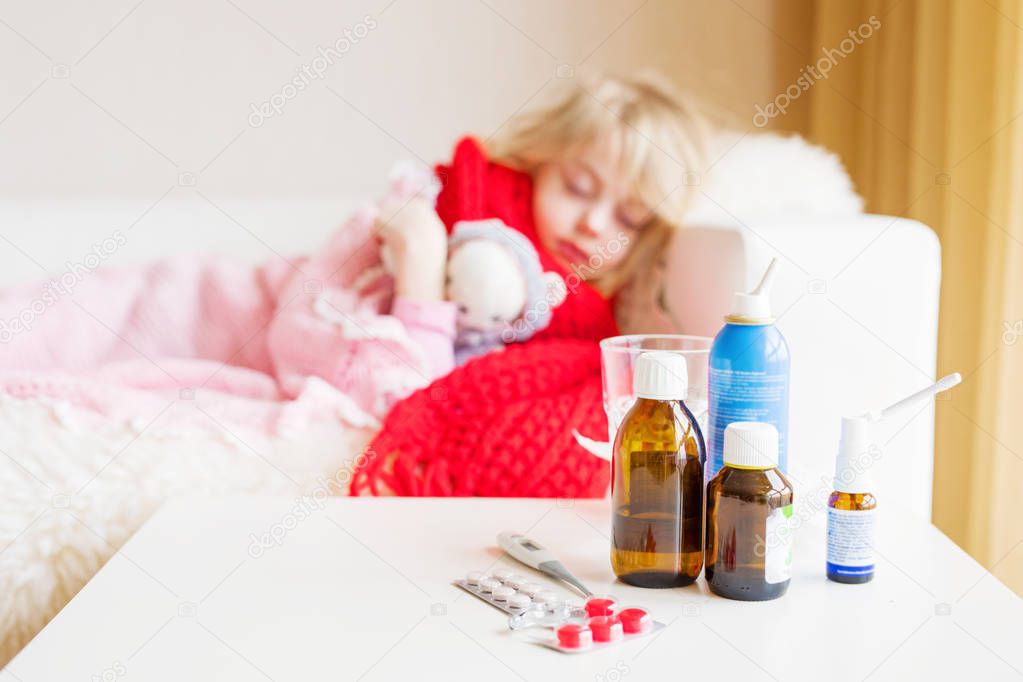 Sick girl lying in bed with medicine bottles in front