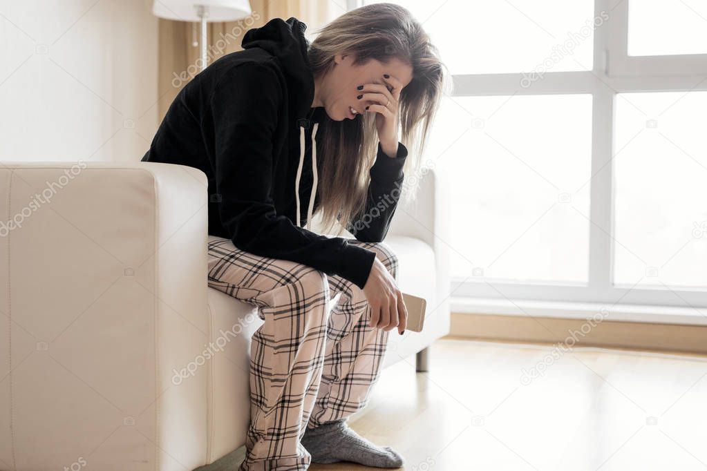 Depressed woman sitting in couch with mobile phone in hand