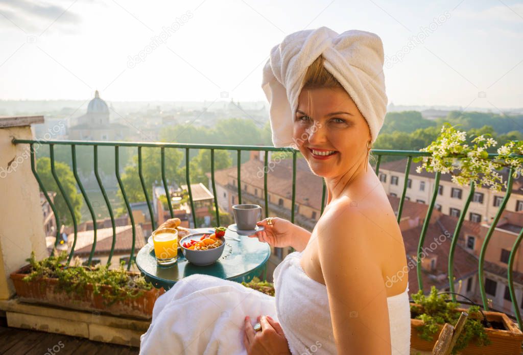 Woman in early morning having breakfast on balcony overlooking city
