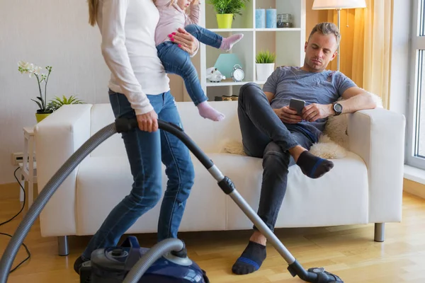 Frau Mit Kleinem Kind Erledigt Hausarbeit Während Mann Auf Couch — Stockfoto