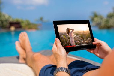 Havuzun yanında tablet film izlerken adam.