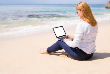 Sahilde dinlenirken bilgisayarda çalışan kadın