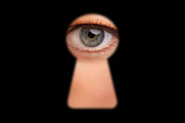 Eye of person looking through keyhole in doors