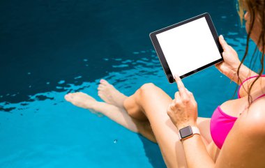 Havuz kenarında oturan ve tablet bilgisayar kullanarak bir kadın. Yatay ekran yukarı alay.