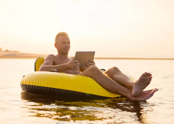 Gün Batımında Suda Şişme Halka Üzerinde Tablet Ile Adam — Stok fotoğraf