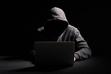 Hacker working on laptop in the dark clipart