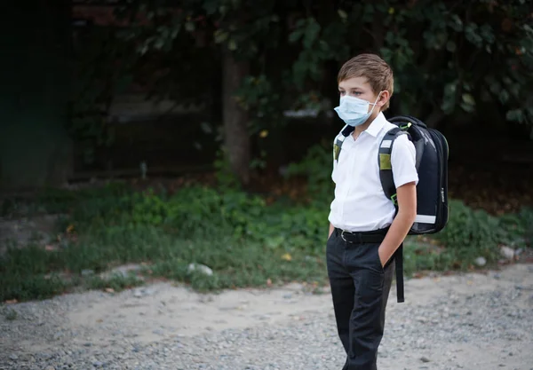 A child of the European race goes to school with a knapsack and a protective medical mask. A schoolboy goes to school in the midst of the COVID-19 pandemic. Go to school wearing masks.