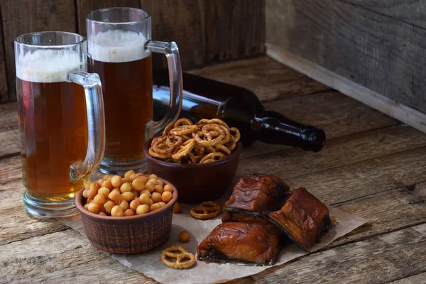 Football fan set with mugs of beer, bottle and salty snacks on wooden background. Junk food for beer or cola. Photographed with natural light. Copy space.