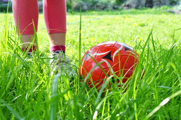 Kızın bacakları ve kırmızı top yeşil çimenlerin üzerinde görünümünü kapatın. Çocuklar oynarken futbol kavramı egzersiz.