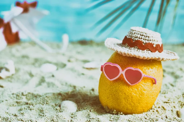 Yaratıcı en az yaz fikir. Bambu şapka, güneş gözlüğü ve plaj şemsiyesi kum içinde limon narenciye hippi. Tropikal plaj kavramı. Yaratıcı sanat. Kopya alanı.