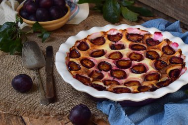 Ahşap arka plan üzerinde beyaz seramik formundaki erik turtası. Homemade Pişirme. Sağlıklı hamur işleri. Vejetaryen yiyecekler. Rustik fotoğraf. Kopya alanı