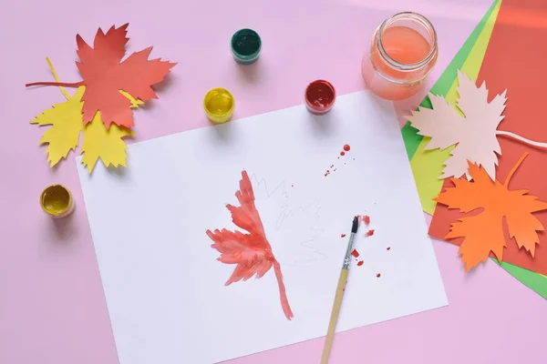 Half-painted maple leaf, paint and brush. Unfinished work. Quitter. Pass of difficulties. Autumn melancholy.