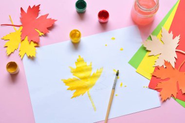 Yarım boyalı akçaağaç yaprağı, boya ve fırça. Yarım kalmış iş. Pes eden biri. Zorlukları geçmek. Sonbahar hüznü.