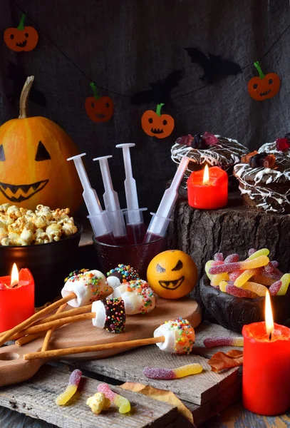 Halloween trick or treat party. Funny delicious sweets and pumpkin on wooden background - muffins, cupcakes, marshmallows, popcorn, juice, jellies, candy