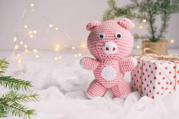 Pink pig, symbol of 2019 and gift on white background. Happy New Year and Merry Christmas card. Crochet toy for child. Handmade crafts on holiday with your own hands. DIY concept. Copy space.