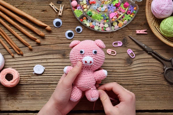 Making pink pig. Crochet toy for child. On table threads, needles, hook, cotton yarn. Step 2 - to sew all details of toy. Handmade crafts. DIY concept. Small business. Income from hobby.