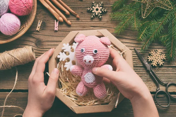 Gift wrapping - pink pig, symbol of 2019. Happy New Year. Crochet toy for child. On table threads, needles, hook, cotton yarn, Christmas decoration. Handmade crafts on holiday. DIY concept