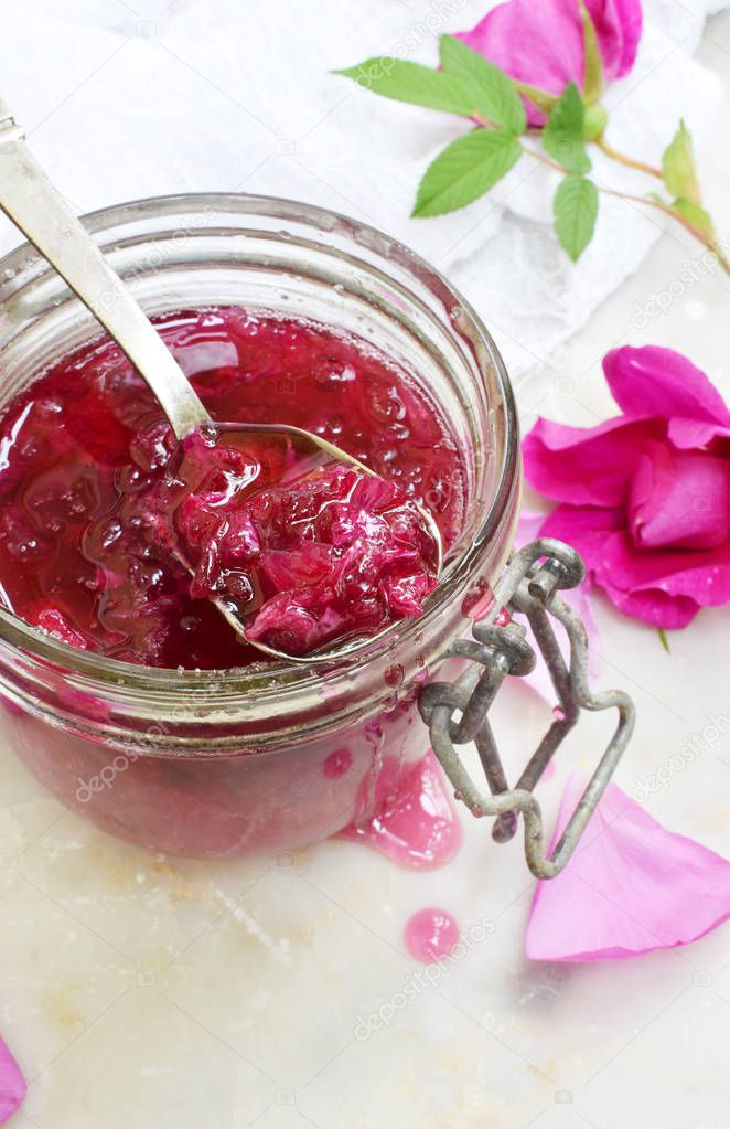 Jam of tea rose petal in glass jar on light marble background. Flower confiture. Healthy food. Copy space.