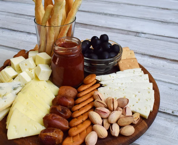 Peynir tabakları grisini ile kraker, tarihleri, reçel, zeytin ve fındık ahşap arka plan üzerinde servis. Peynir kurulu. Şarap için snack.