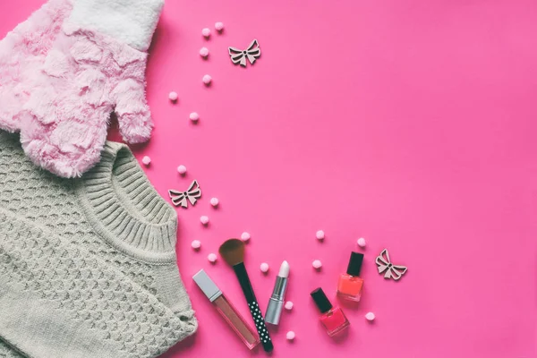 Knitted sweater, warm mittens, nail polishes, lipstick on a pink background. Winter and autumn set of warm, comfortable clothes and makeup cosmetics. Copy space. Top view.