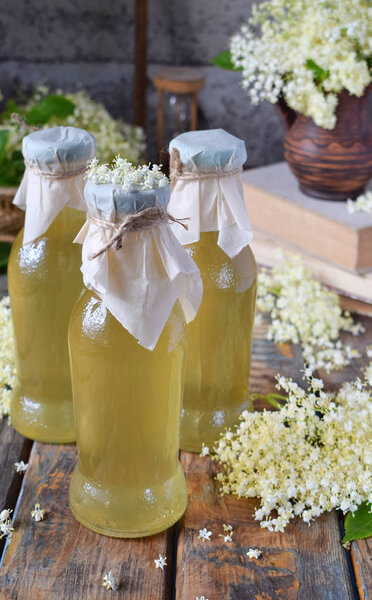 Elderflower cordial syrup and blossom flower in wooden background. Edible elderberry flowers add flavour and aroma to drink and dessert. Copy space.