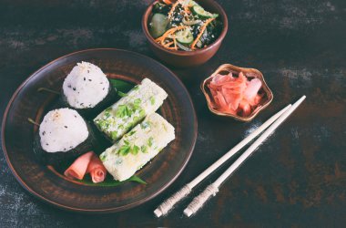 Japon yemekleri - pirinç topları onigiri, omlet, turşu zencefil, sunomono wakame salatalık salatası ve yemek çubukları karışımı. Kahvaltı ve öğle yemeği arka plan