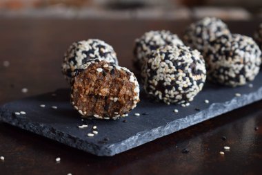 Sağlıklı ham enerji keten tohumu, badem, muz ve tarihleri ile ısırır. Vegan domalan susam koyu arka plan üzerinde içinde. Ev yapımı şeker topları. Çiğ gıda. Ücretsiz Gluten. Süt ücretsiz.