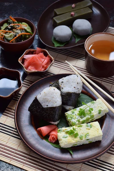 Mezcla de comida japonesa - bolas de arroz onigiri, tortilla, jengibre, ensalada de pepino wakame sunomono. Postre tradicional de frijol y té verde matcha - yokan jalea, mochi daifuku. Desayuno asiático o almuerzo — Foto de Stock