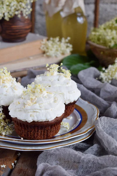 Chocolate capcakes with vanilla cream sprinkled with white chocolate and elderberry flowers. Vintage style. Copy space. — Stock Photo, Image