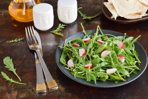 Салат из свежих овощей - руккола, редис, сыр фета в черной тарелке с плоской лепешкой. Здоровое питание — стоковое фото