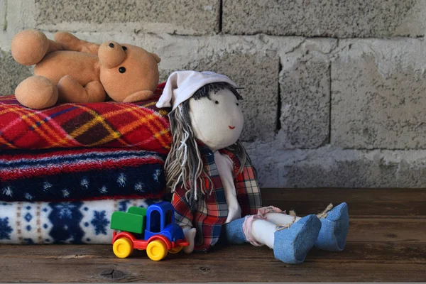 Montón de mantas de lana caliente y muñeca sobre fondo de madera. Juguetes textiles para niños. Comodidad en casa. Juguete hecho a mano. Revestimientos coloridos . — Foto de Stock