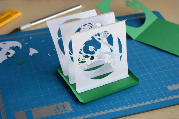 Making tunnelbook. 3D greeting card Spring. Artwork equipment and tools for paper cut - cutting knife, sharp box cutter, blue cutting plate, origami paper. Modern 3d origami paper art style.