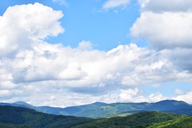 Yeşil çimenler, ormanlarla kaplı dağlar ve bulutlu mavi gökyüzü. Yaz dağ manzarası.