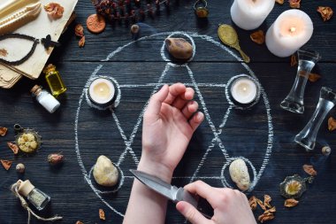 Mumlar, taşlar, aşk iksiri ve cadı masasında eski kitaplar ile pentagram daire üzerinde Kadın elleri ve bıçak. Gizli, ezoterik veya kehanet kavramı. Mistik, Cadılar Bayramı ve vintage arka plan
