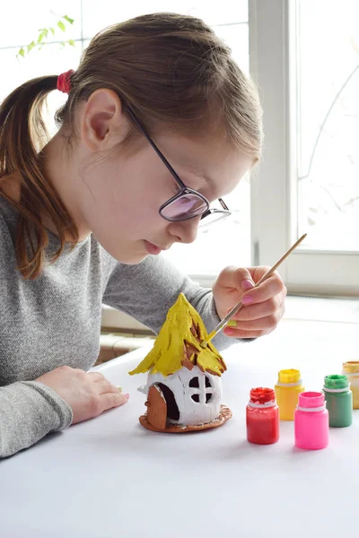 Chica haciendo juguetes con sus propias manos, pinta una casa de barro con gouache. Ocio creativo interior para niños. Apoyo a la creatividad, aprendizaje por hacer, proyecto de bricolaje, artesanía. Clase magistral de arte —  Fotos de Stock