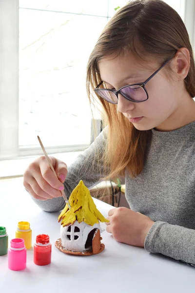 Chica haciendo juguetes con sus propias manos, pinta una casa de barro con gouache. Ocio creativo interior para niños. Apoyo a la creatividad, aprendizaje por hacer, proyecto de bricolaje, artesanía. Clase magistral de arte —  Fotos de Stock