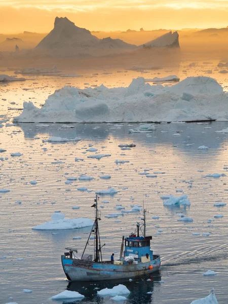 一艘格陵兰岛渔船在融化的海冰中穿行 背景上漂浮着被橙色落日照射的冰山 气候危机 — 图库照片