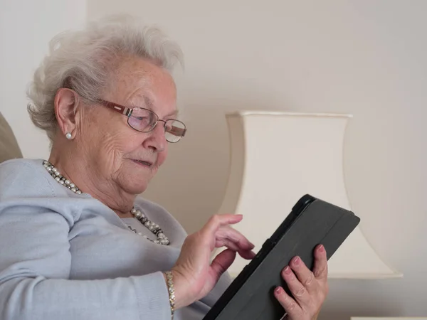 Yaşlı bir kadın bakarken gülümsüyor ve tabletine dokunuyor.