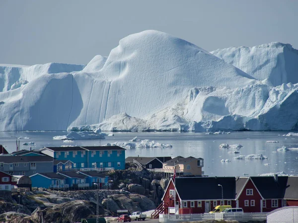 在绿地的一个传统渔村后面 可以看到一个巨大的冰川 在海湾里 融化的海冰在漂浮 — 图库照片