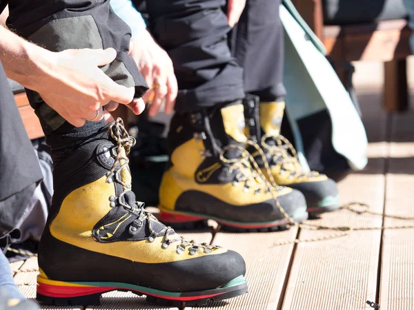 A mountaineering boot has been laced up and hands are folding trousers over them.A colourful striped sole is designed to take crampons