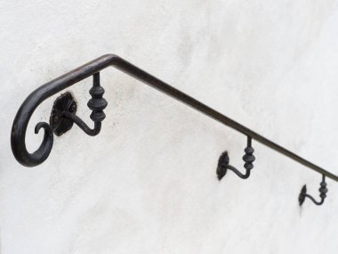 Süslü siyah metal bir el parmaklığı çapraz mesafeye doğru gidiyor. Beyaz boyalı bir duvara sabitlenmiş. Odaklanma noktası dar.