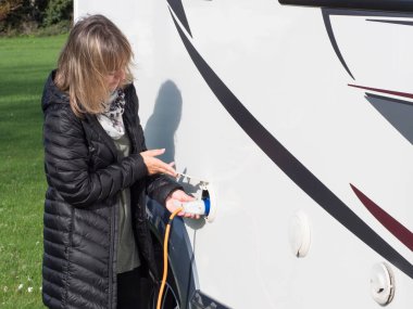 Bir bayan kapağı kaldırıyor ve karavana güç sağlamak için turuncu bir elektrik kablosu takıyor.