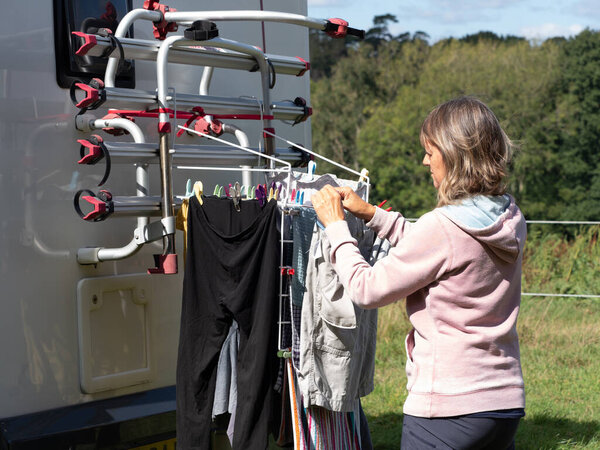A lady motorhome owner hangs washing on her bike rack to dry with a rural scene in background