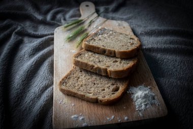 Ekmek mutfak tahtasına ve buğday dallarına konur. Bir bardak süt var.