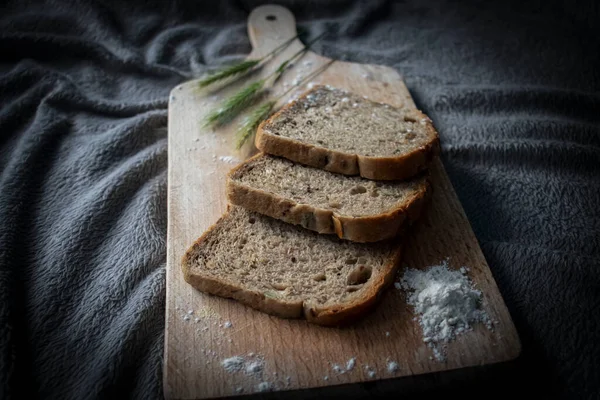 Ekmek mutfak tahtasına ve buğday dallarına konur. Bir bardak süt var.