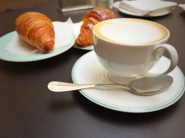 Kapuçino beyaz Kupası, kruvasan karanlık retro arka plan, seçici odak üzerinde. Kahvaltı konsepti